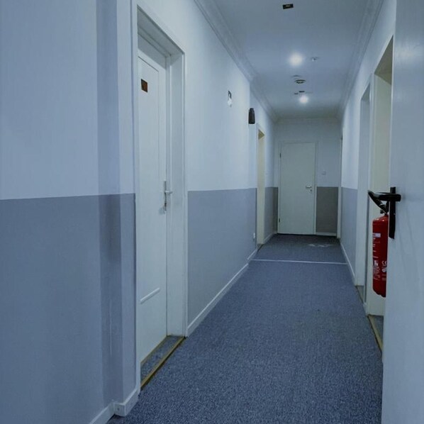 A corridor with white and grey walls, doors, and a blue carpet. - Hotel Tyros am Weidendamm (Hannover)
