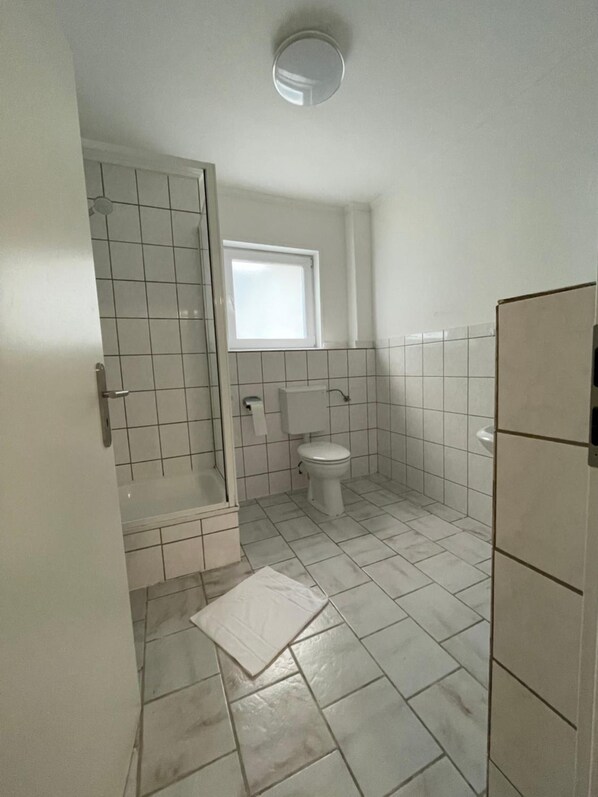 A small, clean bathroom with a toilet, a shower, and a window. - Hotel Tyros am Weidendamm (Hannover)