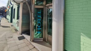 A hotel entrance with a glass door, a metal awning, and a green brick wall. - Hotel Tyros am Weidendamm (Hannover)