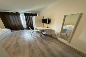 A small, modern room with a wooden floor, a desk, two chairs, a television, and a large mirror. - Hotel Tyros am Weidendamm (Hannover)