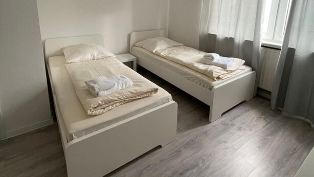 A small, clean room with two single beds, a window with curtains, and a radiator. - Hotel Tyros am Weidendamm (Hannover)