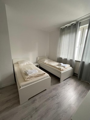 A small, clean room with two single beds, a window with curtains, and a radiator. - Hotel Tyros am Weidendamm (Hannover)