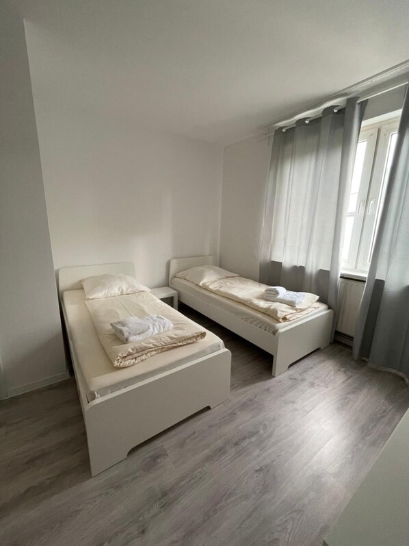 A small, clean room with two single beds, a window with curtains, and a radiator. - Hotel Tyros am Weidendamm (Hannover)