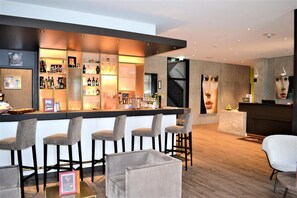 A bar area with a counter, bar stools, and a seating area with a table and chairs. - Hotel am Campus (Ingolstadt)
