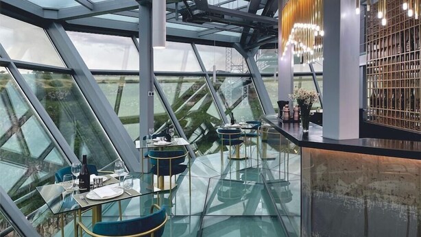 A modern restaurant with glass tables and chairs, a high ceiling, and a view of the cityscape. - Kass Diamond Resort (Tsalka)