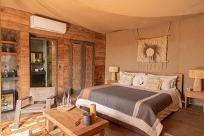 Ein Schlafzimmer mit einem hölzernen Bett, einem Nachttisch, einem Tisch mit Kerzen, einem Wandbehang aus Makramee und einem Regal mit Flaschen.