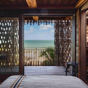 A room with a bed, a view of the beach, and a wooden door. - Nomade Holbox (Isla Holbox)
