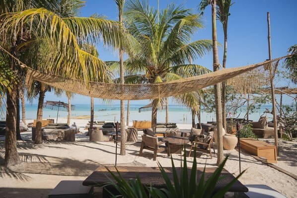 Eine Strandlounge mit Außenbestuhlung, Palmen und Blick auf das Meer.