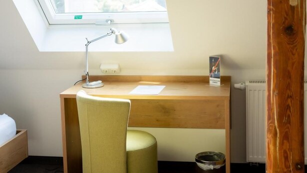 A room with a skylight, a desk, a chair, a radiator, and a trash bin. - Lahn Hotel (Biedenkopf)