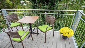 A wooden deck with a table and two chairs, a metal railing, and a potted plant with yellow flowers. - Lahn Hotel (Biedenkopf)