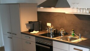 Une cuisine moderne avec des meubles blancs, une cuisinière noire, un évier en acier inoxydable et une hotte aspirante.