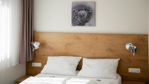 Une chambre d’hôtel avec une tête de lit en bois, deux lampes de chevet, un lit blanc avec deux oreillers et une œuvre d’art accrochée au mur.