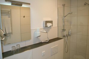 A modern bathroom with a large mirror, a towel rack, a hairdryer, and a shower. - Lahn Hotel (Biedenkopf)
