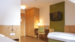 Ein Hotelzimmer mit zwei Betten, einem Schreibtisch, einem Stuhl, einem Fernseher und einem Kleiderschrank.