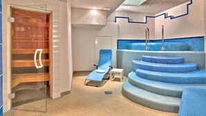 Ein Spa-Raum mit einer Holztür, einem blauen Massagesessel und einem Pool mit Trepeneinheit.