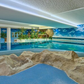 Una piscina interior con un mural tropical, una formación rocosa y vista a un cielo azul claro.