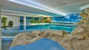Ein Hallenbad im tropischen Stil, mit Felsformationen und einem Wandgemälde einer Strandlandschaft.