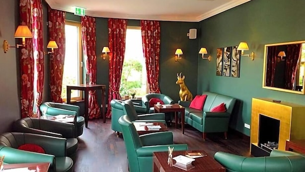 A hotel lobby with green sofas, a fireplace, and a deer statue. - Campus Garden Businesshotel (Iserlohn)
