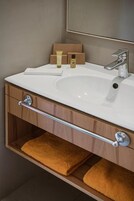 Un baño con un lavamanos blanco, un espejo, un perchero para toallas y un estante con artículos de aseo.