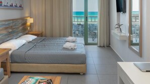 Een hotelkamer met een bed, een bureau, een televisie en een balkon met uitzicht op zee.