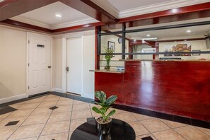 Een hotel lobby met een receptiebalie, een potplant en een deur met de tekst 'Entrance'.