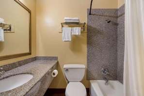Baño con lavamanos y encimera de granito, inodoro, ducha con pared de granito y un perchero con toallas.