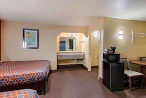 A hotel room with a bed, a small kitchenette, a dining table, and a mirror. - New Orleans East Hotel (New Orleans)