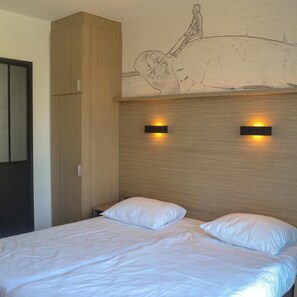 Een slaapkamer met een houten hoofdbord, twee bedlampjes en een groot bed met witte beddengoed.