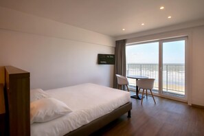 Een hotelkamer met een bed, een bureau en een stoel. Er is een groot raam met uitzicht op zee.