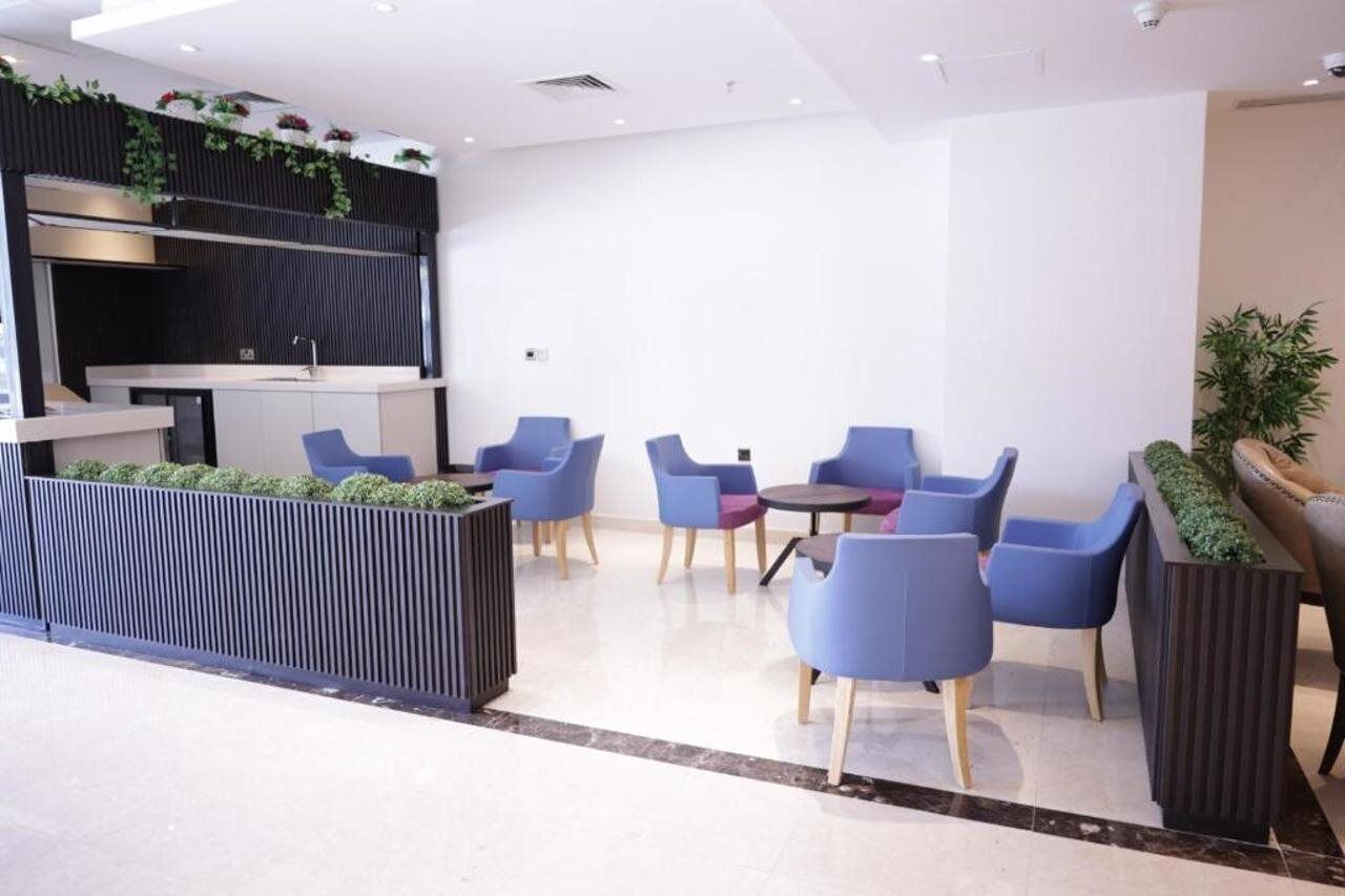 Un espace de détente moderne avec des sièges bleus, un comptoir d’accueil noir et un jardin vertical.