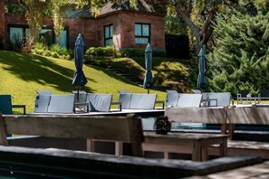 A patio area with outdoor seating and umbrellas, a brick building in the background, and a well-maintained lawn. - Be House Suites & Spa by Nobile (Punta del Este)