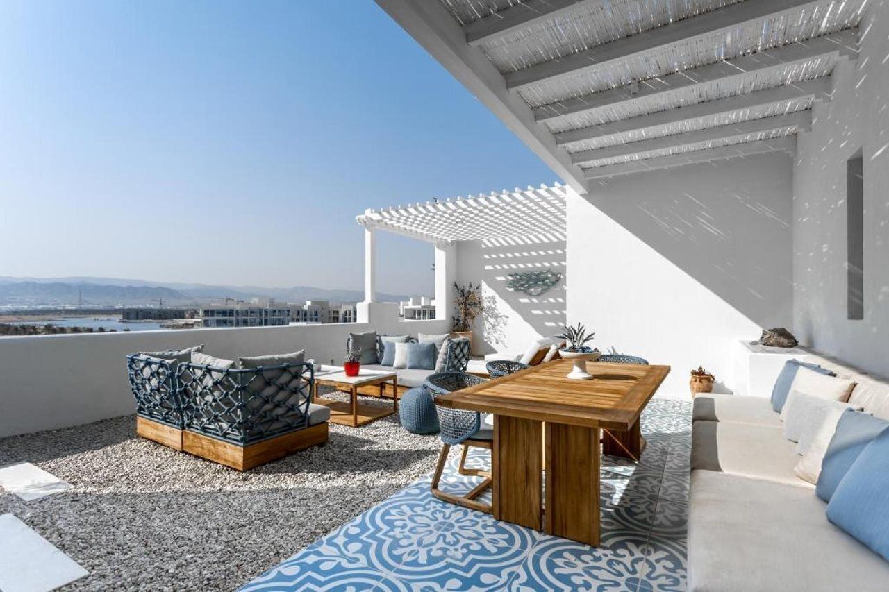 A rooftop terrace with a white pergola, seating area with cushions and a table, and a view of distant mountains.