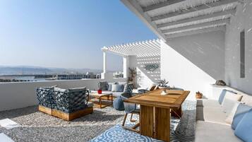 A rooftop terrace with a white pergola, seating area with cushions and a table, and a view of distant mountains.