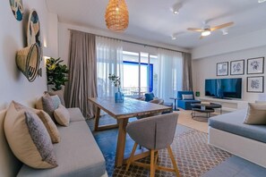 A modern living room with a wooden dining table, a sofa, a TV, and a ceiling fan. - Cloud7 Residence Ayla Aqaba (Aqaba)