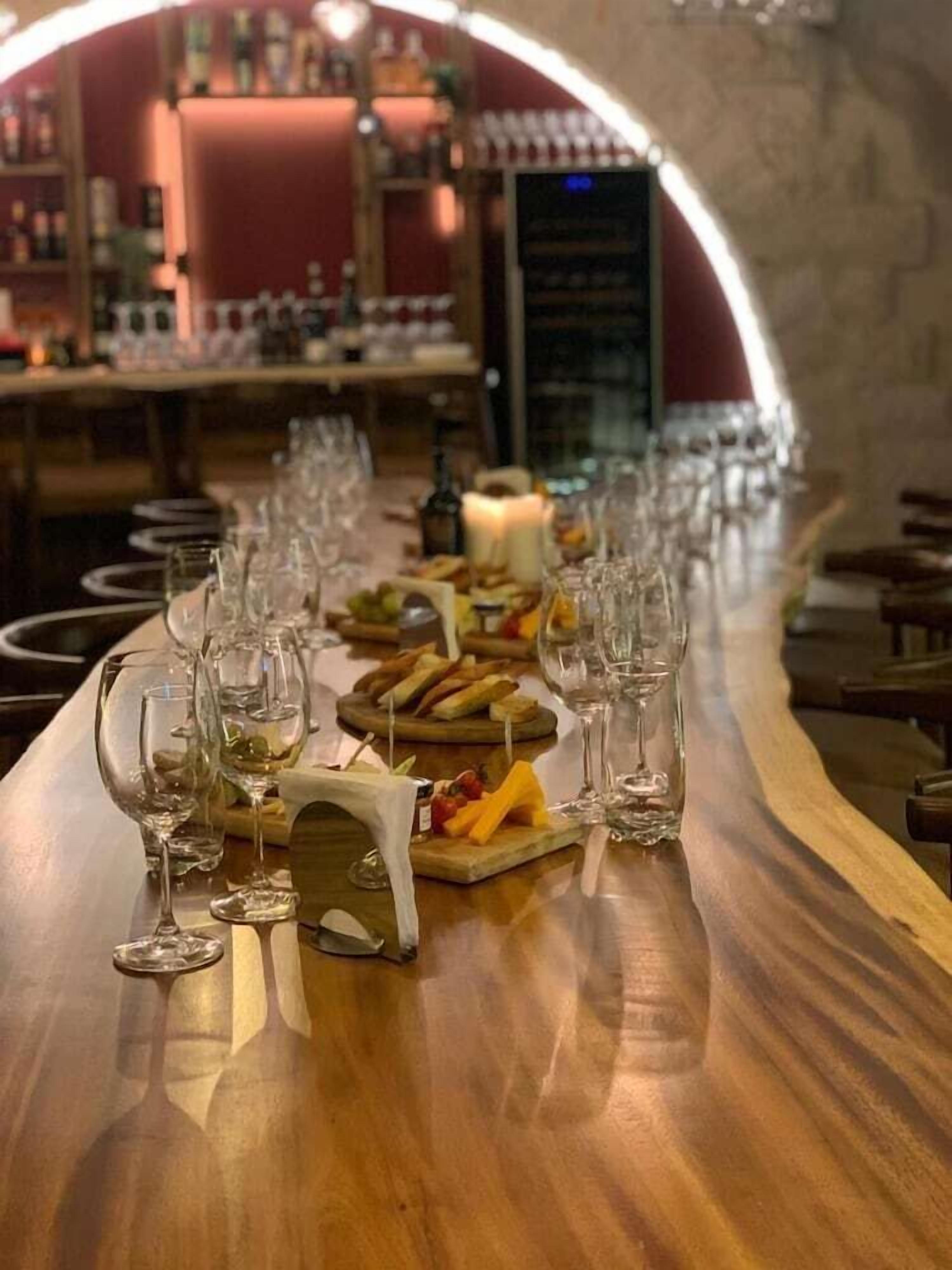 A long bar with multiple wine glasses and a variety of cheeses and fruits on a wooden table.