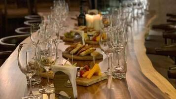 A long bar with multiple wine glasses and a variety of cheeses and fruits on a wooden table.