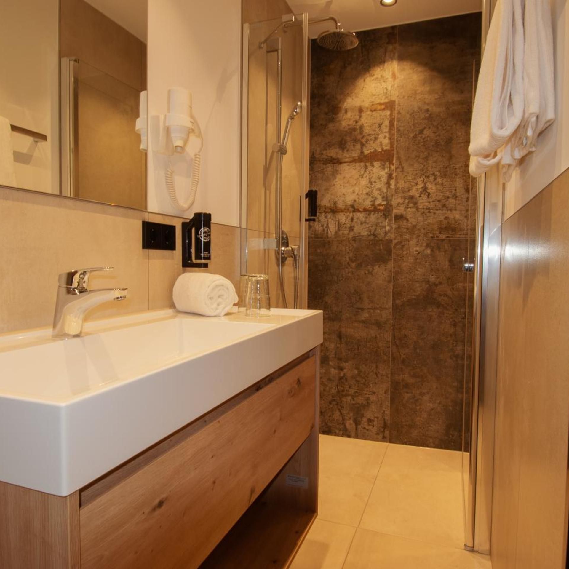 A modern bathroom with a white sink, wooden vanity, a glass shower enclosure, and a towel rack.