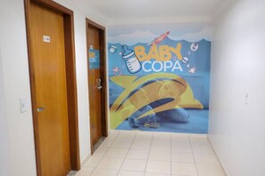 A hallway with a baby-themed mural on the wall, two wooden doors, and a tiled floor. - Suite Para ATE 4 Pessoas EM Golden Dolphin Grande Hotel Piscina 24h (Caldas Novas)