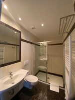 Un baño con lavamanos blanco, inodoro y cabina de ducha con mampara de vidrio.