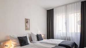 Een hotelkamer met twee bedden, een klein bureau, een stoel en een raam met gordijnen.