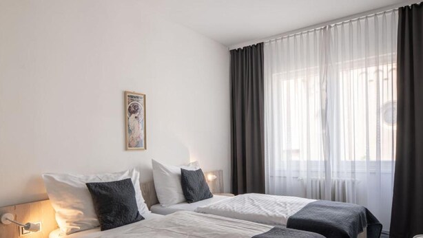 Een hotelkamer met twee bedden, een klein bureau, een stoel en een raam met gordijnen.