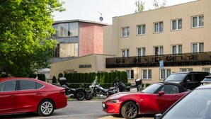 Een hotel met een modern ontwerp, herkenbaar aan het platte dak en de grote ramen. Voor het gebouw staan diverse geparkeerde auto's en motorfietsen.