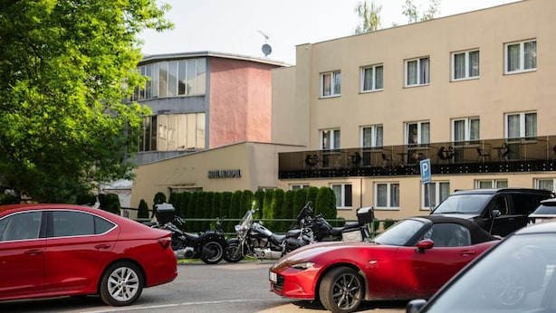 Il s’agit d’un hôtel au design moderne, caractérisé par un toit plat et de grandes fenêtres. Plusieurs voitures et motos sont garées devant le bâtiment.
