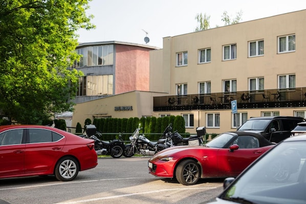 Il s’agit d’un hôtel au design moderne, caractérisé par un toit plat et de grandes fenêtres. Plusieurs voitures et motos sont garées devant le bâtiment.