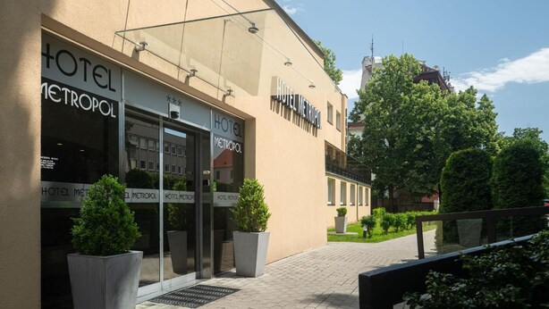 Een hotelentree met een moderne gevel, grote ramen en plantenbakken.