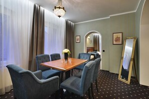 Une chambre d’hôtel avec une table à manger, quatre chaises, un vase avec des fleurs, un lustre, un miroir et un papier peint à rayures.