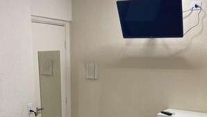 A hotel room with a bed, a small refrigerator, a TV mounted on the wall, and a cabinet. - Hotel Jurubatuba (São Bernardo do Campo)