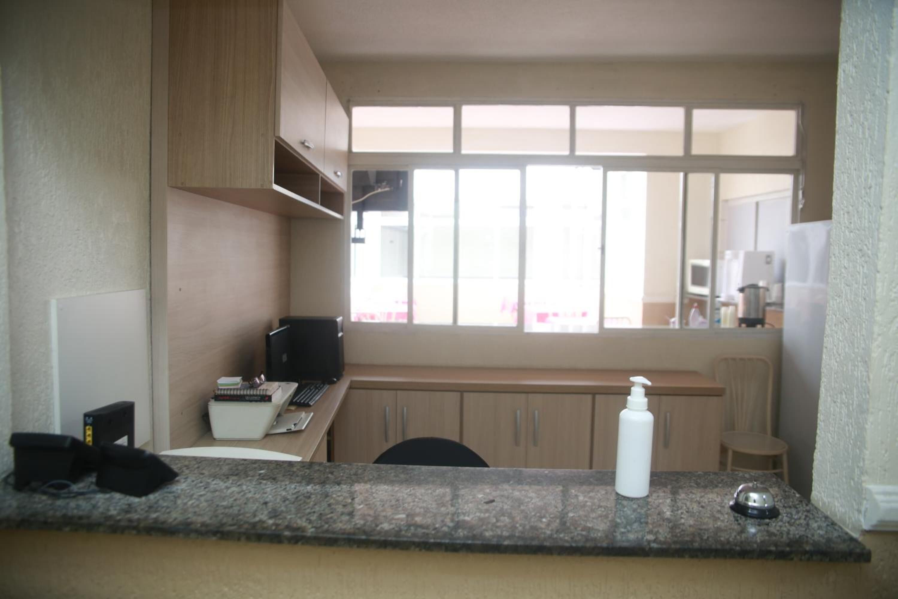 A small kitchenette with a countertop, a sink, and a window with curtains.