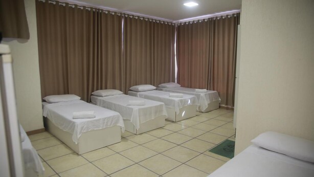 A hotel room with four single beds arranged in a row, a tiled floor, and curtains on the windows. - Hotel Jurubatuba (São Bernardo do Campo)