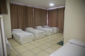 A hotel room with four single beds arranged in a row, a tiled floor, and curtains on the windows. - Hotel Jurubatuba (São Bernardo do Campo)
